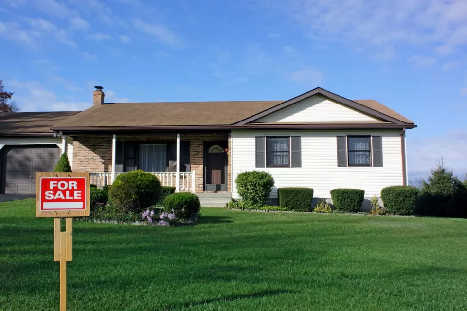 Small home with For Sale sign on green lawn.